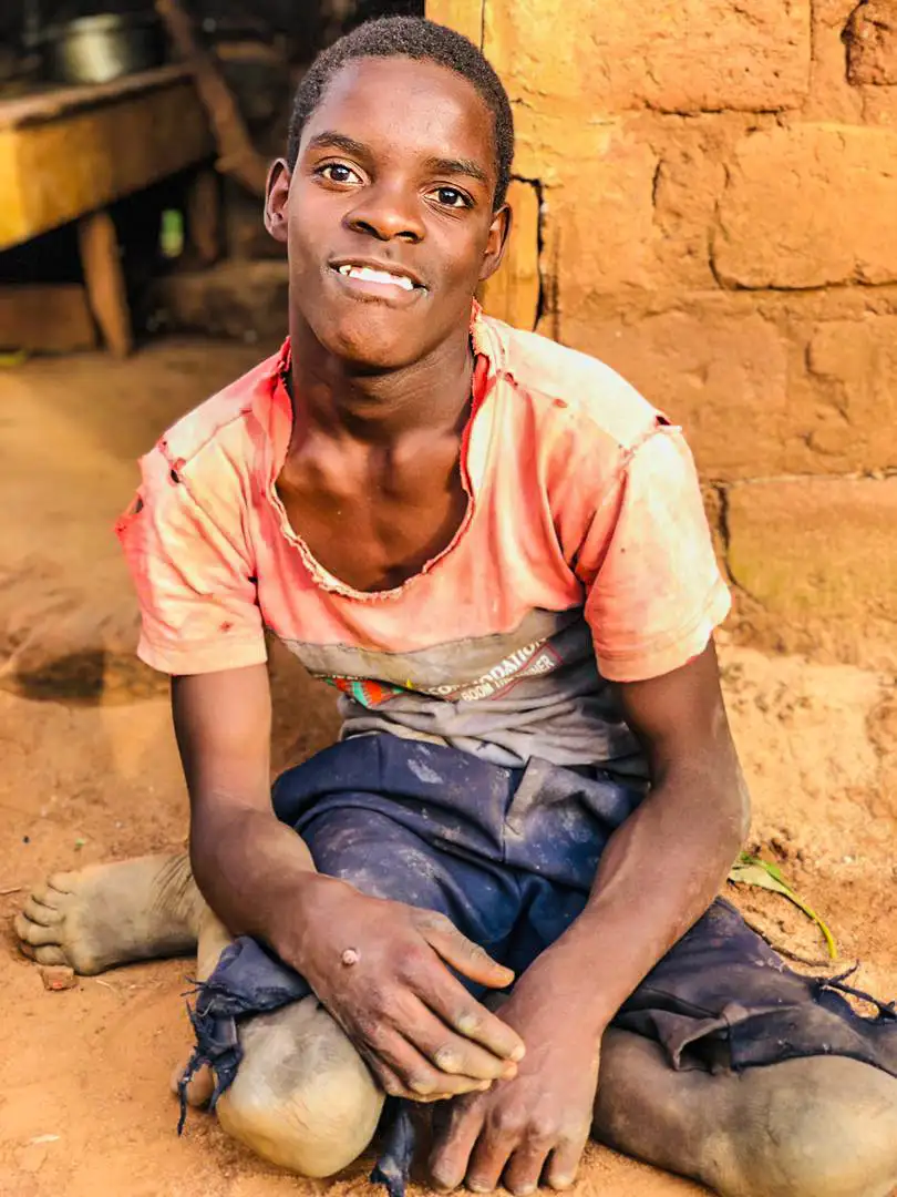 A young man in Uganda smiling with dignity while seated on the ground